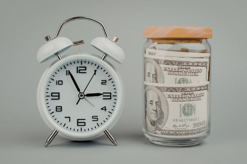 Alarm clock beside a jar of cash representing strategic timing of RMDs to lower taxes in retirement.