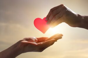 Hands passing a heart, representing charitable giving through required minimum distributions and qualified charitable distributions.